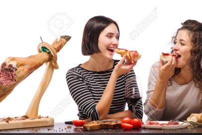 Two girls eat slices of meat and drink wine. Isolated over white background